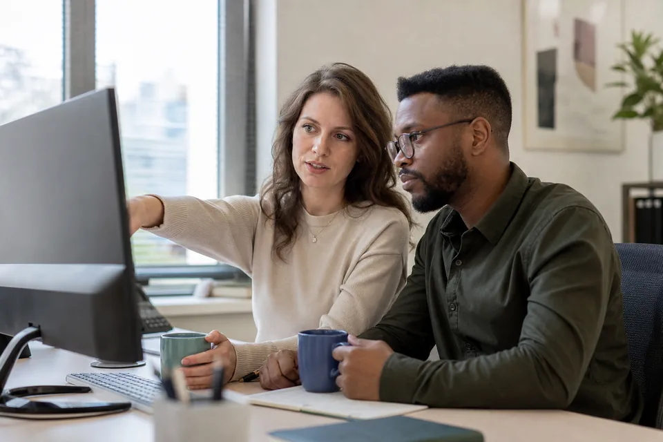 Two staffing agency recruiters reviewing candidate profiles together on a large monitor